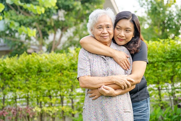 Anciana asiática con hija de cuidador caminando y abrazo con feliz en el parque natural.