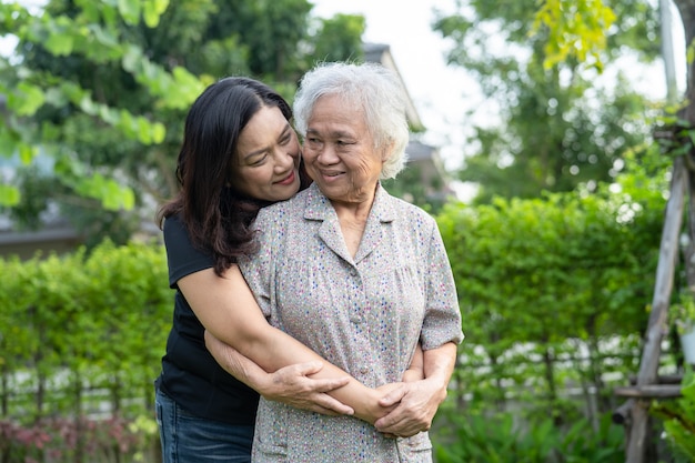 Anciana asiática con hija de cuidador caminando y abrazo con feliz en el parque natural.