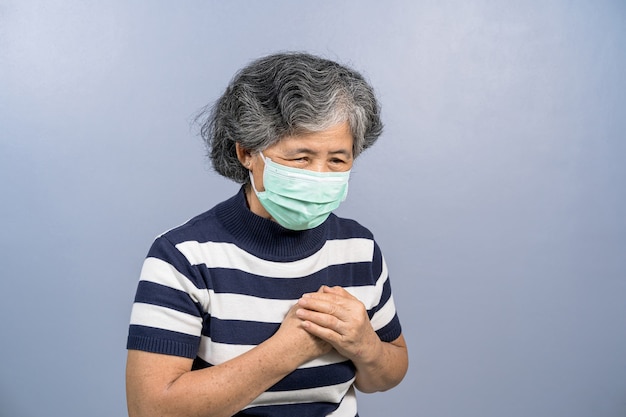 Anciana asiática con mascarilla quirúrgica facial y sensación de dolor al tocar el pecho con corazón