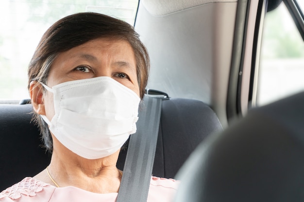 Una anciana asiática pasajera usa una máscara quirúrgica para prevenir el coronavirus o Covid-19 mientras está sentada en el automóvil. virus pandémico en el transporte público.