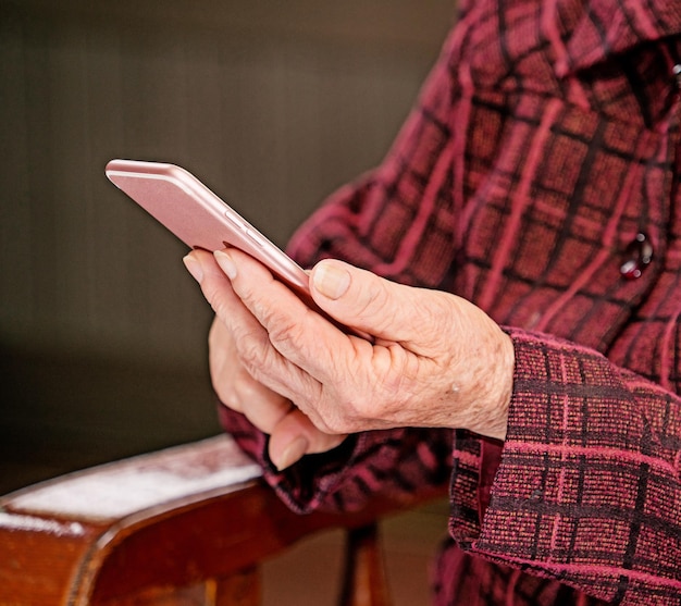 Anciana asiática sentada y mirando a través de algo en un teléfono inteligente moderno que se conecta con otros en casa tecnología de vida cercana