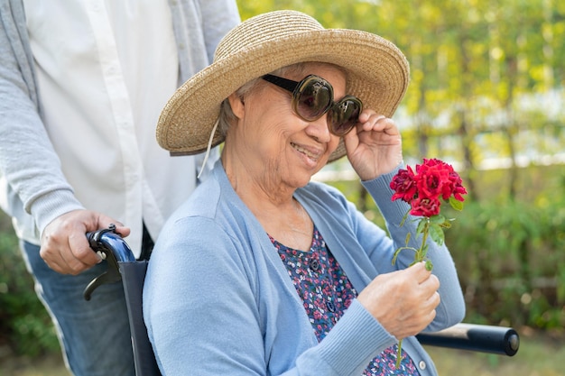 Anciana asiática con una sonrisa de flor de rosa roja y feliz en el jardín soleado