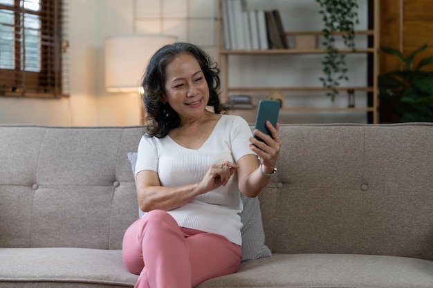 Anciana asiática usando teléfono celular y sentada en un sofá en casa