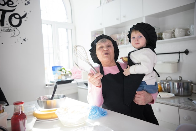 Una anciana con un batidor de pie en la cocina con una niña en las manos