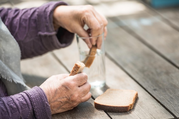 La anciana bebe agua y come pan en una vieja mesa de madera en un jardín.