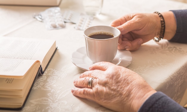 Anciana beber bebida caliente en casa. Senior pensionista mujer sosteniendo la taza de café en sus manos