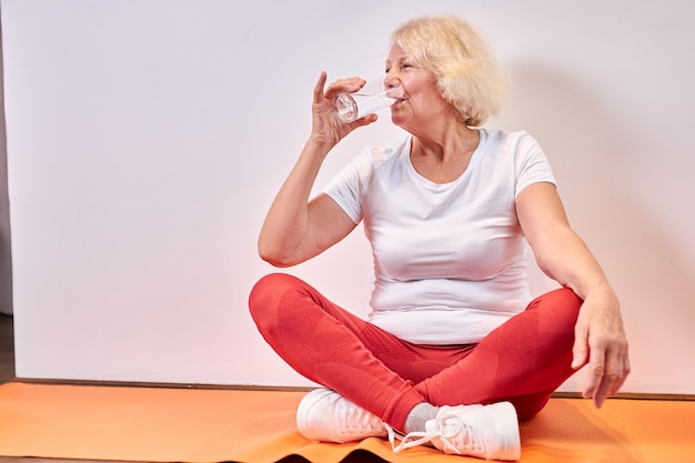Anciana bebiendo agua dulce después de ejercicios deportivos en el suelo, descansar. concepto de estilo de vida saludable