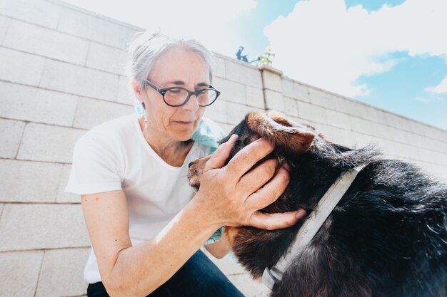 Anciana besando y mirando a un perro con amor, durante un día soleado y brillante