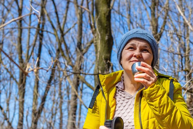 Una anciana en el bosque de la primavera está bebiendo té. Mujer feliz en la naturaleza