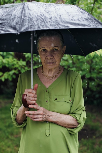 Una anciana se para en la calle bajo la lluvia con un paraguas negro