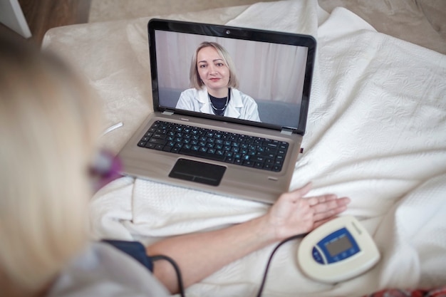 Anciana en la cama mirando la pantalla de la computadora portátil y consultando con un médico en línea en casa, telesalud