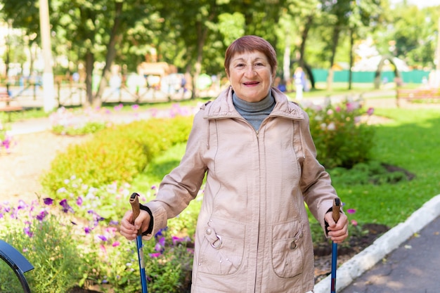 Una anciana camina nórdico con palos en el parque en un día soleado de verano