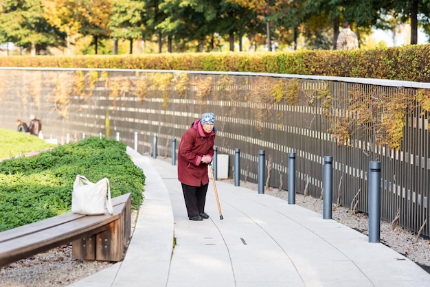 Una anciana camina en el parque encorvada vestida con un abrigo rojo