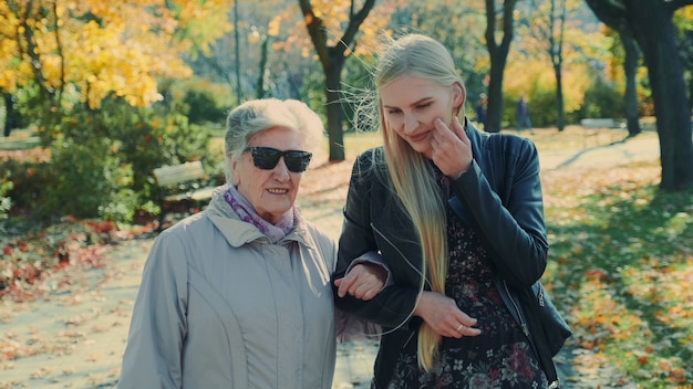 Anciana caminando junto a la alegre chica rubia en el parque otoño