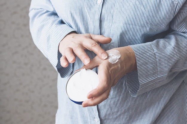 Una anciana con una camisa azul se aplica crema en las manos