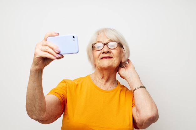 Anciana en una camiseta amarilla posando comunicación por teléfono de fondo claro