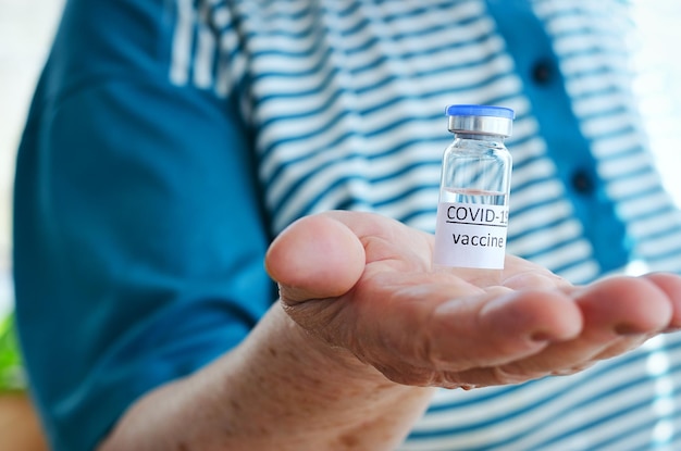 Anciana con camiseta azul sosteniendo una botella de vidrio de vial de vacuna para la vacunación contra COVID-19.