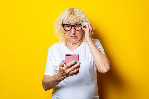 Anciana en camiseta blanca con gafas mirando teléfono