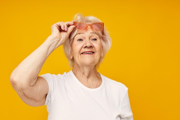 Anciana en una camiseta blanca lleva gafas de fondo amarillo