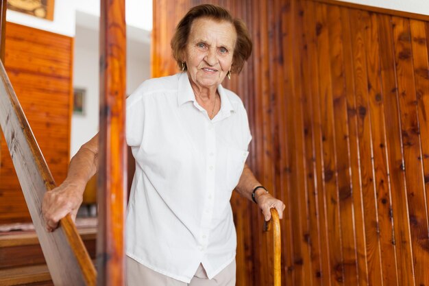 Anciana en casa usando un bastón para bajar las escaleras