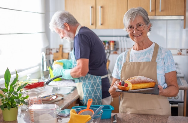 Anciana caucásica en la cocina de la casa muestra con orgullo un plumcake casero recién horneado