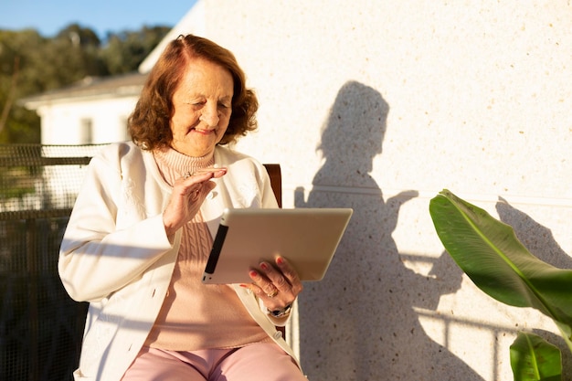 Anciana caucásica haciendo una videollamada desde una tableta digital en la terraza de su casa Concepto de personas mayores y nuevas tecnologías