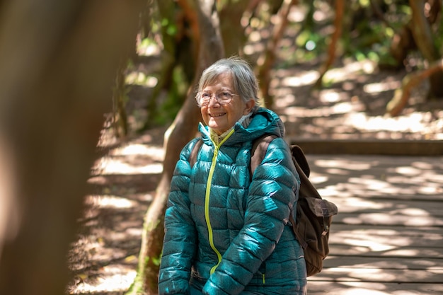 Una anciana caucásica sonriente sentada en el bosque para descansar mirando la belleza de la naturaleza