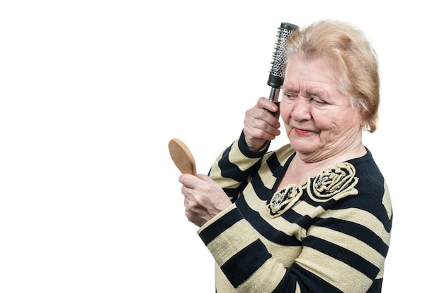 Anciana cepillando su cabello frente a un pequeño espejo de madera aislado sobre fondo blanco.