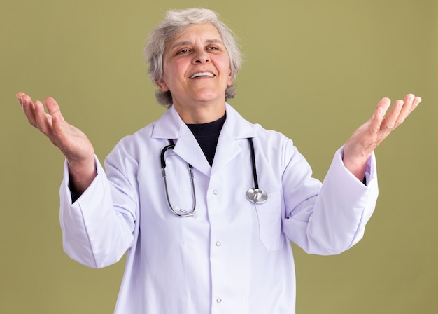 Anciana complacida en uniforme médico con estetoscopio sosteniendo las manos abiertas mirando al lado