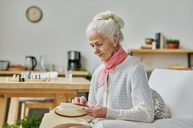 Anciana concentrándose en su artesanía sentada en un sillón y bordando