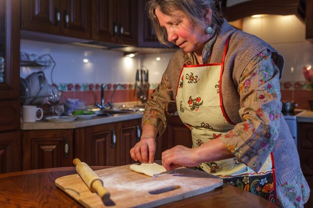 Una anciana con delantal prepara pasteles en la cocina