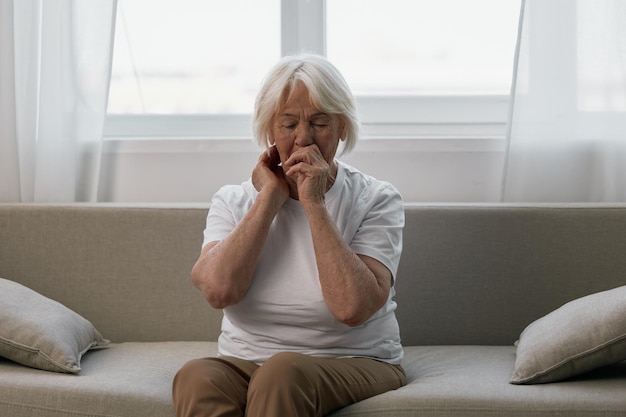 Foto anciana dolor de dientes severo sentado en el sofá problemas de salud en la vejez mala calidad de vida abuela con canas sostiene su mandíbula dolorida