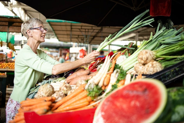 Anciana eligiendo y comprando verduras saludables en el mercado.