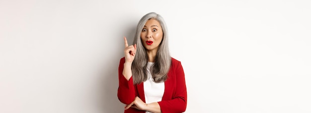 Anciana empresaria asiática con chaqueta roja que tiene una idea que sugiere algo levantando el dedo