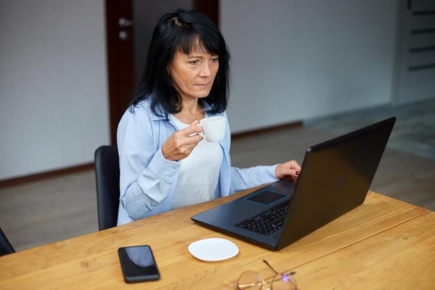 Anciana empresaria relajándose en el lugar de trabajo bebiendo café