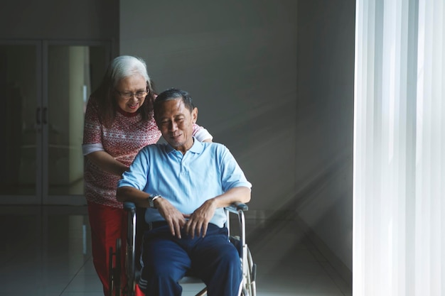 Una anciana empuja a su marido en silla de ruedas.