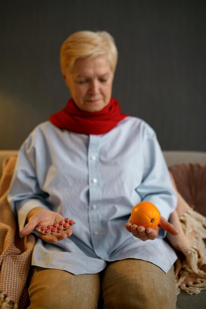 La anciana enferma decide qué elegir naranja o pastillas. Tratamiento médico versus consumo de frutas orgánicas