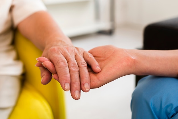 Anciana y enfermera cogidos de la mano de cerca