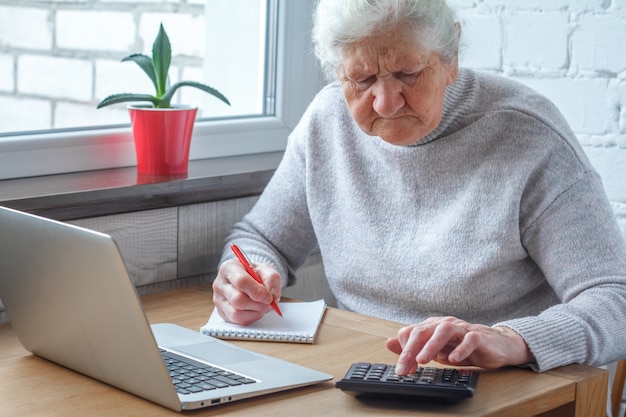 Una anciana está sentada en la mesa frente a la computadora portátil.