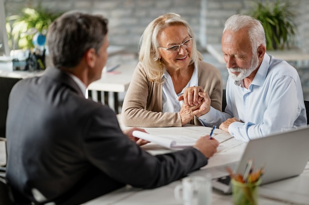 Una anciana feliz anima a su marido a firmar un contrato con el director de su banco durante una reunión en la oficina