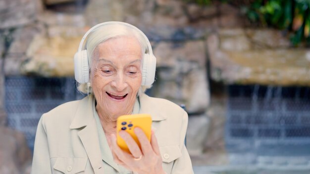 Una anciana feliz escuchando música con auriculares y móvil