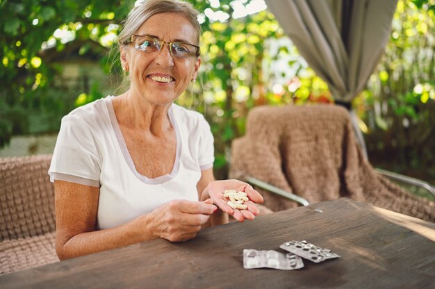 Anciana feliz senior anciana en anteojos recetados toma medicamentos medicamentos vitaminas píldoras al aire libre en el jardín. Concepto de estilo de vida de personas de edad avanzada