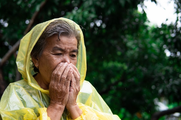 La anciana en gabardina tosiendo durante la lluvia.