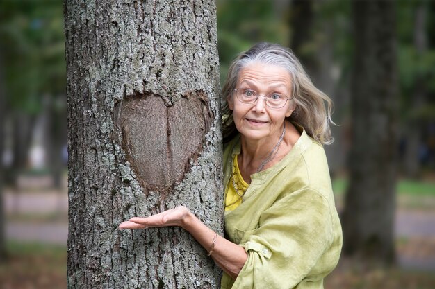 Anciana con gafas muestra con sorpresa el corazón formado por la caída de la corteza en el tronco de un árbol