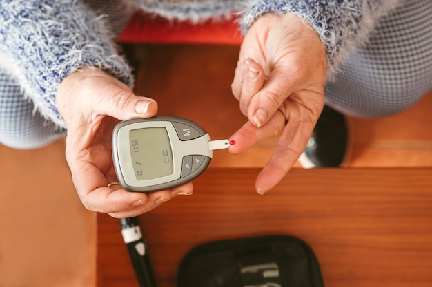 Una anciana con una gota de sangre en el dedo está a punto de colocarla en el medidor de glucosa en sangre Diabetes