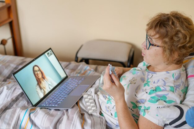 Foto una anciana habla con un médico por skype. un pensionista sufre una enfermedad respiratoria y se suena la nariz. consulta online.