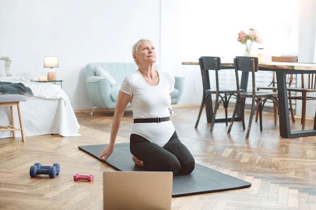 Anciana haciendo ejercicio con un entrenador en línea en el concepto de su sala de estar de un estilo de vida saludable