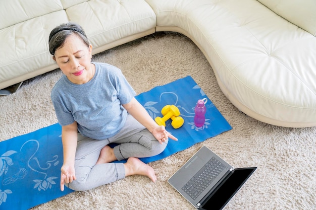 Anciana haciendo ejercicio de yoga usando laptop