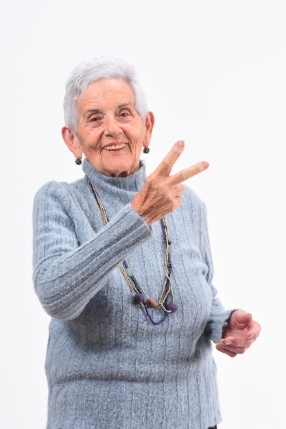 Foto anciana haciendo el signo de la victoria sobre un fondo blanco.