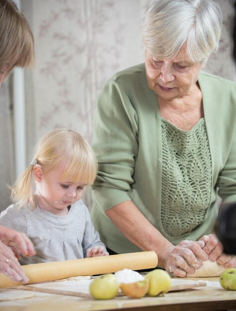 Una anciana haciendo tartas con su nieta enrollando la masa